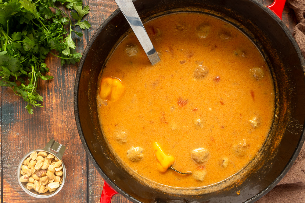 Overhead shot of peanut soup with meatballs in dutch oven with ladle.