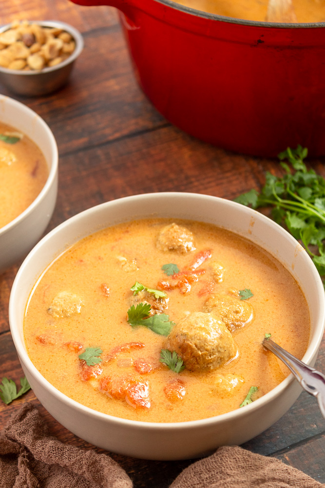 Angled shot of african peanut soup with meatballs in bowl with spoon.