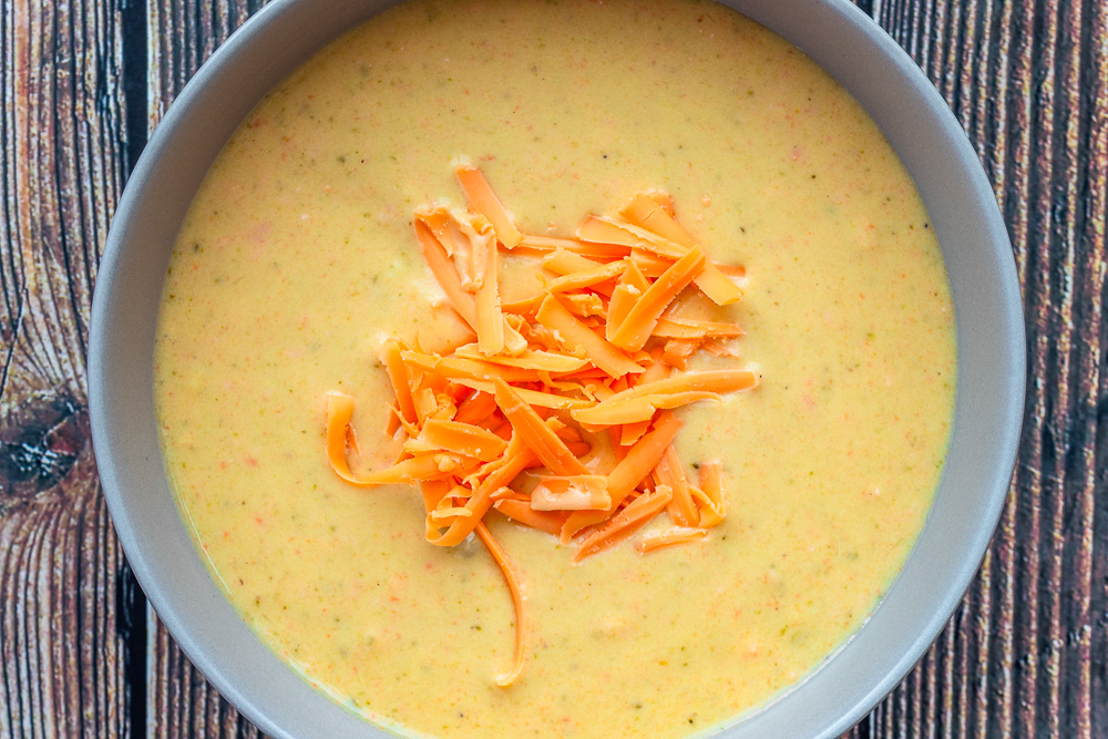 Broccoli cheddar soup overhead shot in a bowl with shredded cheese on top.
