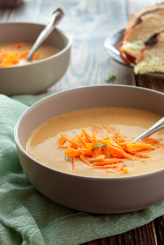 Broccoli cheddar soup in a bowl with shredded cheese on top. Angled shot with back lighting.