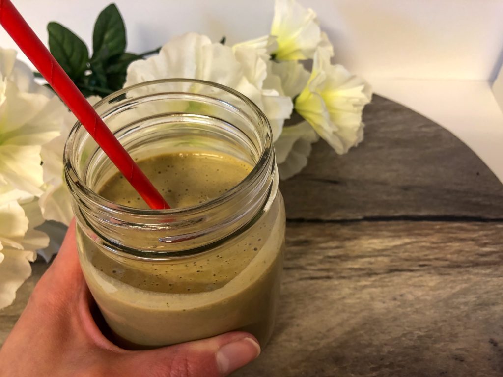 chocolate protein green smoothie with hand and flowers on wooden board