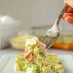 Bacon, broccoli and cheese egg bake on plate with a hand holding a forkful in foreground.