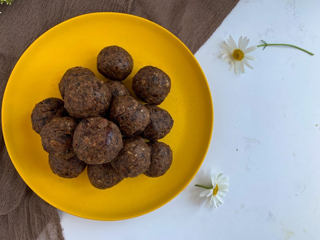 peanut butter date balls stacked on plate beside daisy's