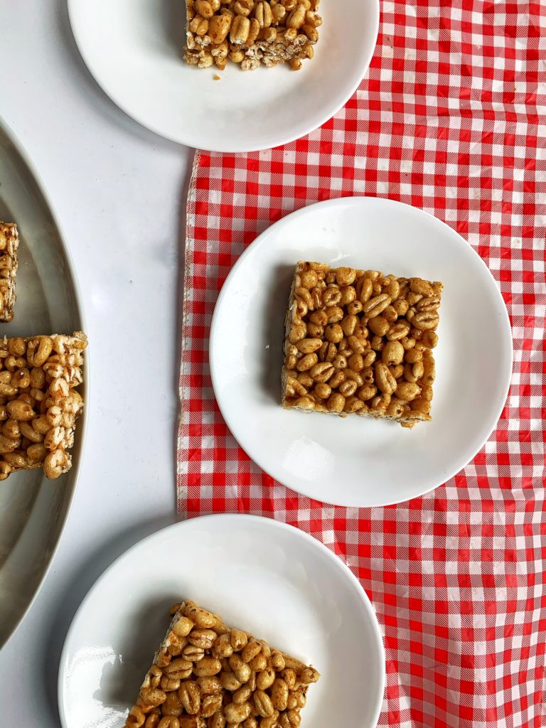 Three Puffed Wheat Squares on individual plates on top of red checkered table cloth. Overhead shot. 