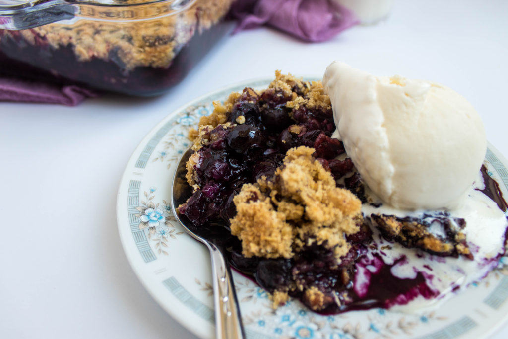 blueberry crisp with oats on plate with ice cream and spoon.