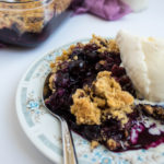 blueberry crisp with oats on plate with ice cream and spoon.