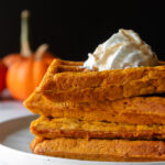 Straight on shot of pumpkin spice waffles on plate with whipped cream. Mini pumpkins in background.