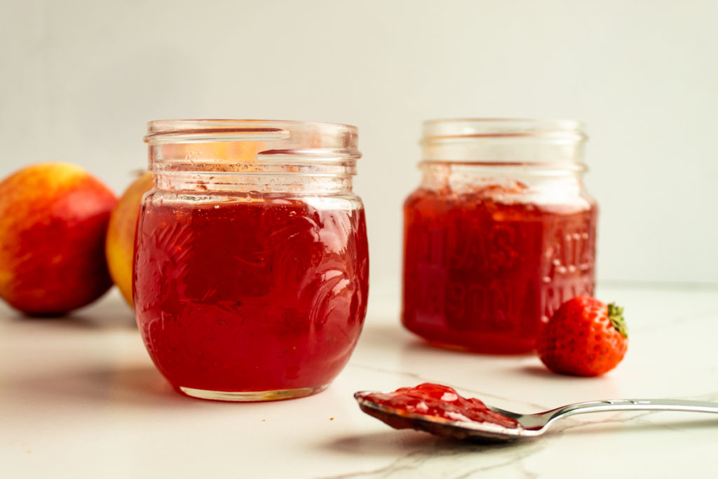 2 open jars of apple strawberry jam with a spoon