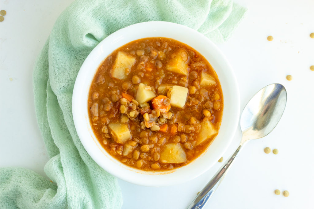 lentil stew in bowl beside spoon overhead shot