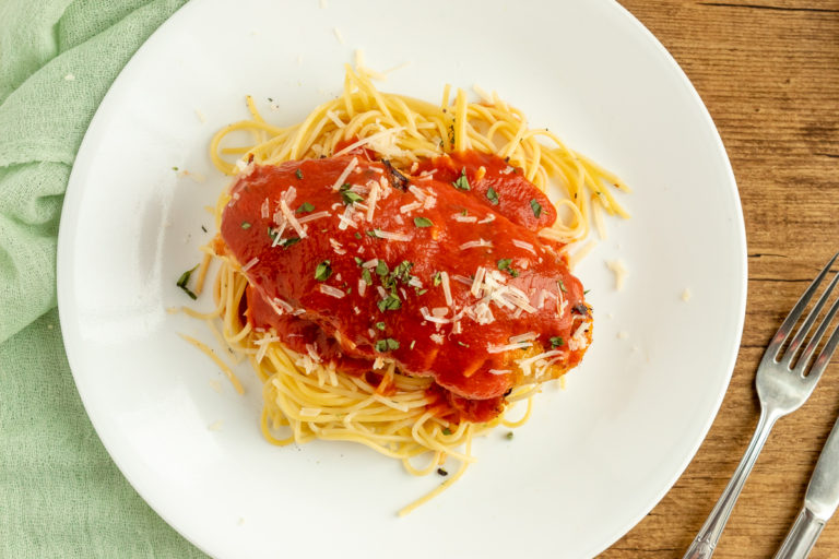 chicken parmesan over spaghetti noodles covered with tomato sauce on plate overhead shot.