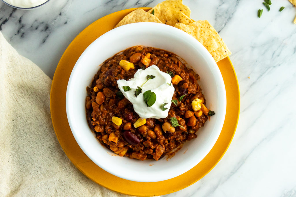 Slow cooker chilli in bowl over plate with chips overhead shot