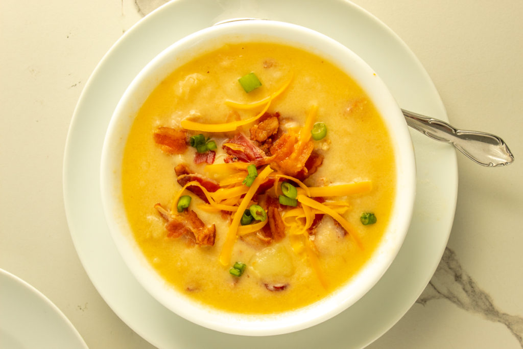 Pressure cooker potato soup overhead shooting bowl over plate with spoon.