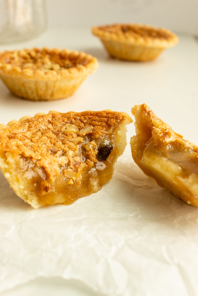 Super Easy Butter Tarts on parchment paper split in half showing gooey centre.