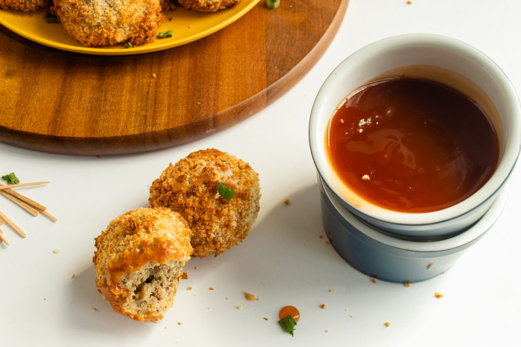 Air fryer chicken balls beside bowl of sweet and sour sauce