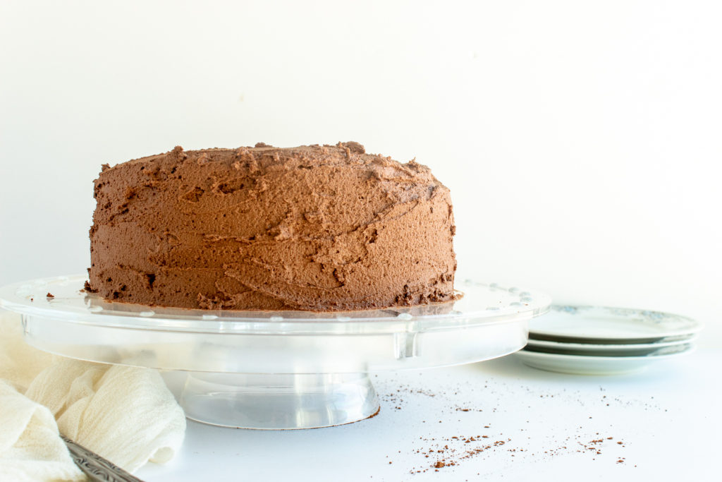 Chocolate layer cake on clear cake stand straight shot.