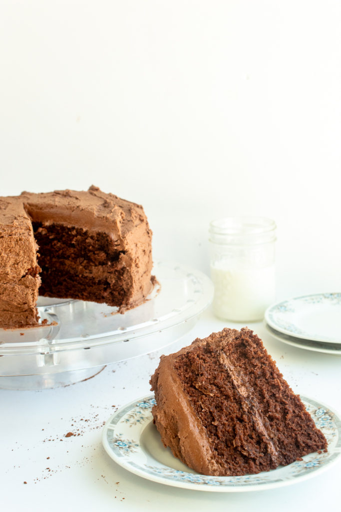 Best Chocolate layer cake on clear cake stand with slice taken out on plate.