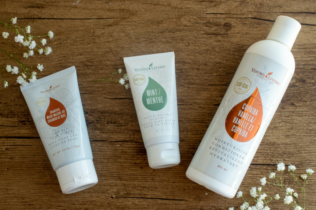 Young Living body care products lying down on wooden placemat overhead shot. Charcoal face mask, Satin facial scrub, and Copaiba Vanilla conditioner just some of my Summer 2021 favourites.