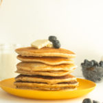 Healthy Whole Wheat Pancakes stacked on yellow plate with butter and blueberries straight on shot.