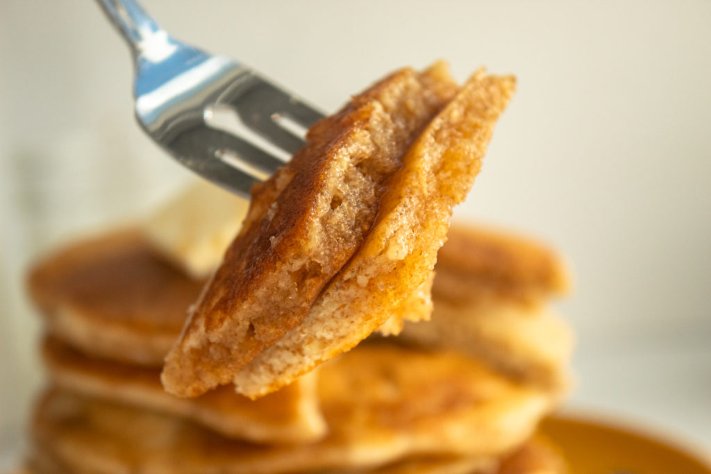 Close up shot of healthy whole wheat pancakes with fork and bites of pancake.