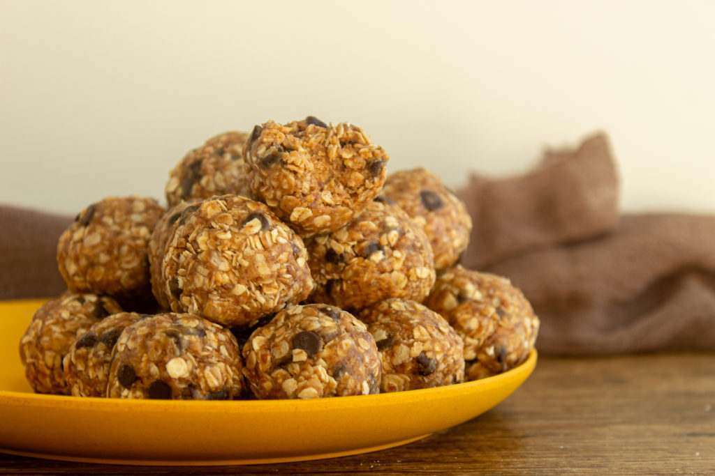 Healthy no bake energy balls stacked on yellow plate with bite out of one.