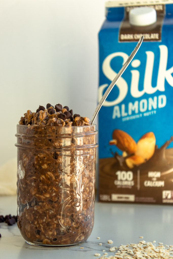 Chocolate peanut butter overnight oats in mason jar with spoon. Silk dark chocolate almond milk in background. 