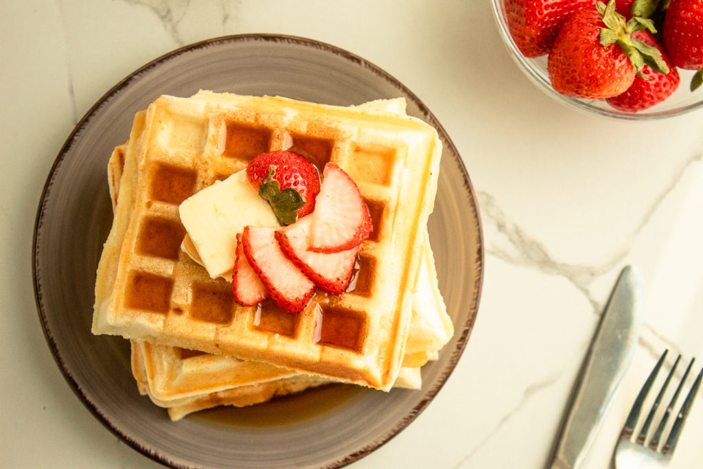 Overhead shot of Soft and fluffy waffles stacked on plate with butter and strawberries on top