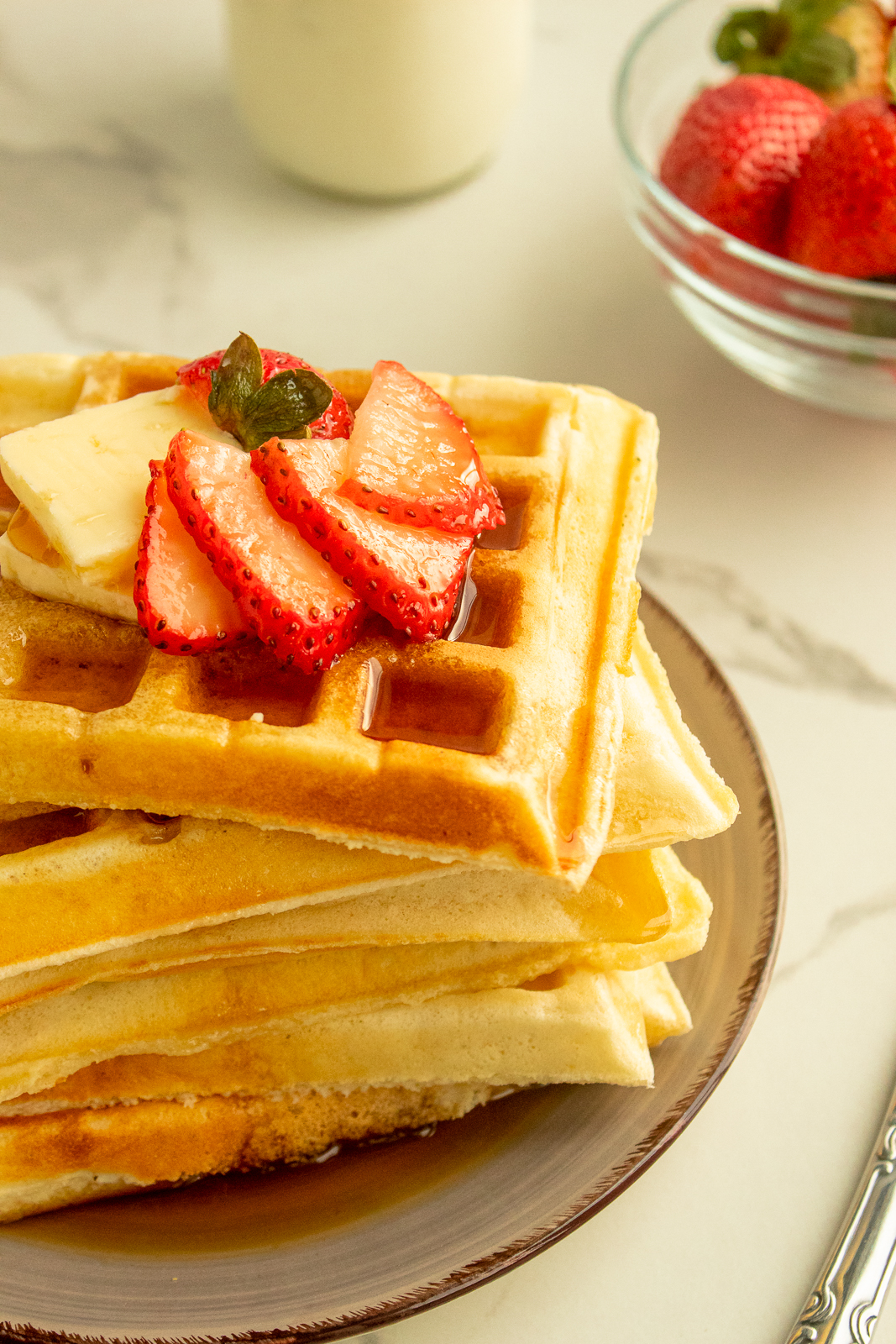 Soft and fluffy waffles stacked on plate with butter and strawberries on top angled shot