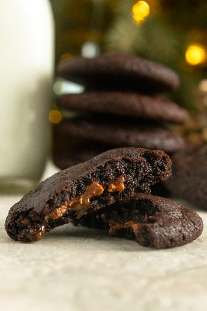 Rolo Cookie in half close up with stack of cookies in background beside glass of milk.