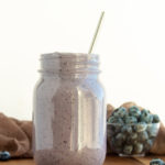 Post workout pb & jelly smoothie in glass mason jar with straw on wooden background with blueberries surrounding.