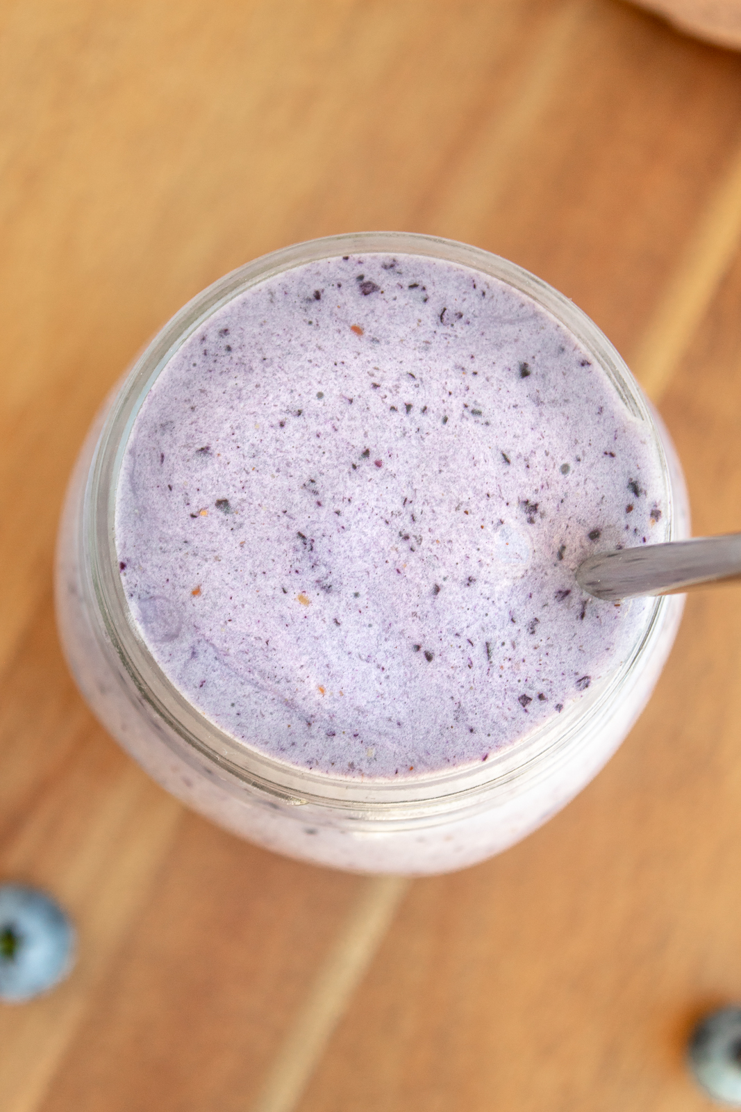 Post workout pb & jelly smoothie in glass with straw overhead shot with wooden background.