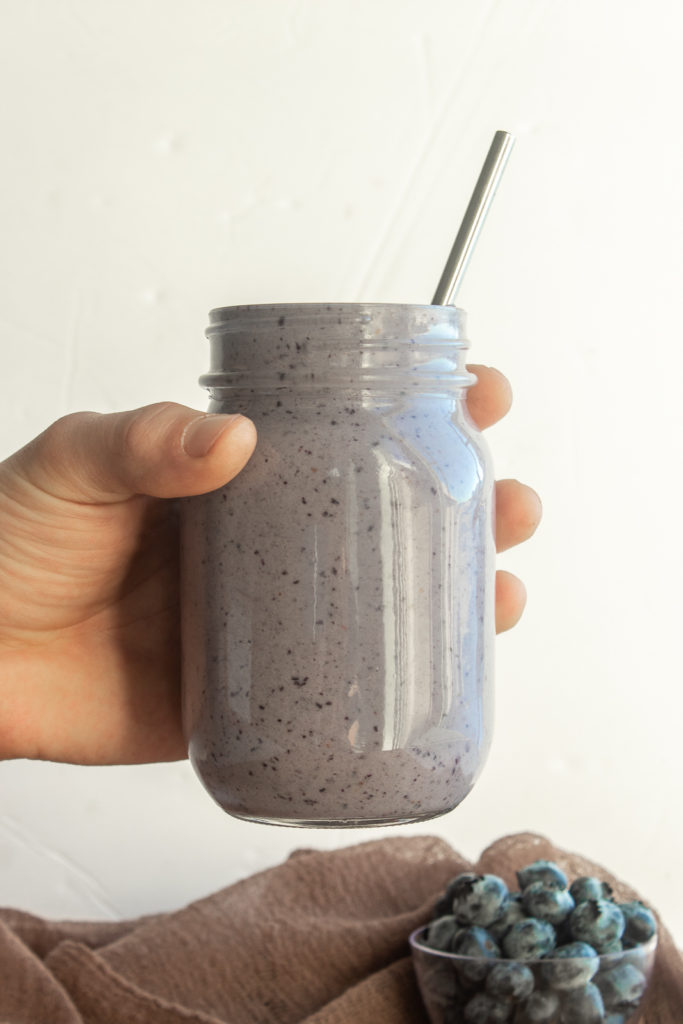 Hand holding Post workout pb & Jelly Smoothie on white background with blueberries.