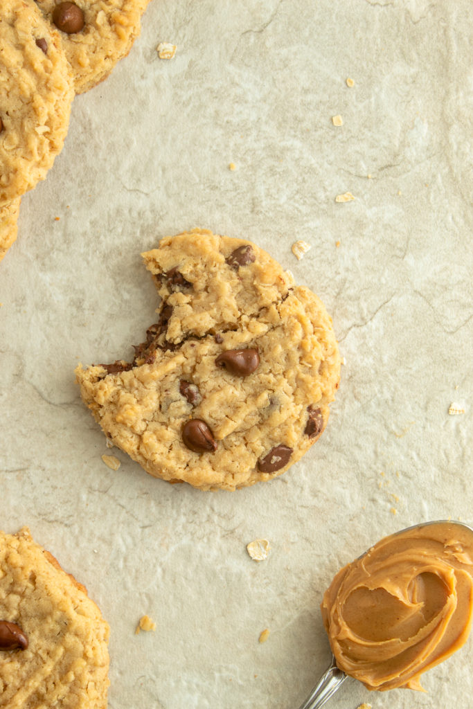 Peanut butter oatmeal chocolate chip cookies overhead shot with bite taken out and spoon full of peanut butter.