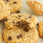 Angled shot of Peanut butter oatmeal chocolate chip cookies with bite taken out and a spoon full of peanut butter in background.