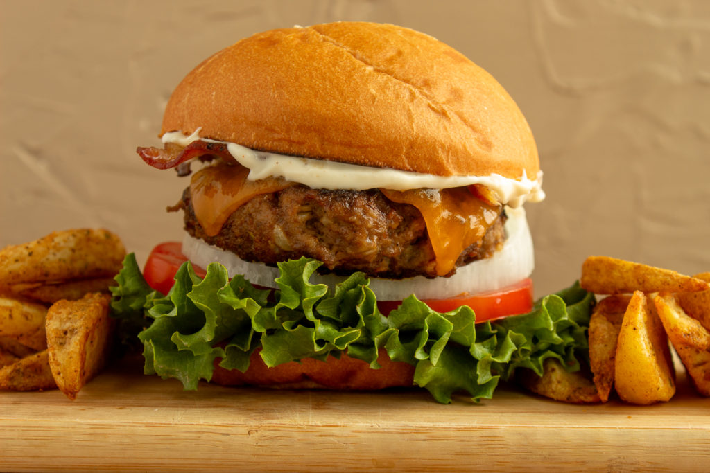 Perfect basic burger on cutting board beside potato wedges straight on shot.