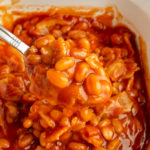 Angled shot of baked beans in casserole dish with a spoonful in the centre.