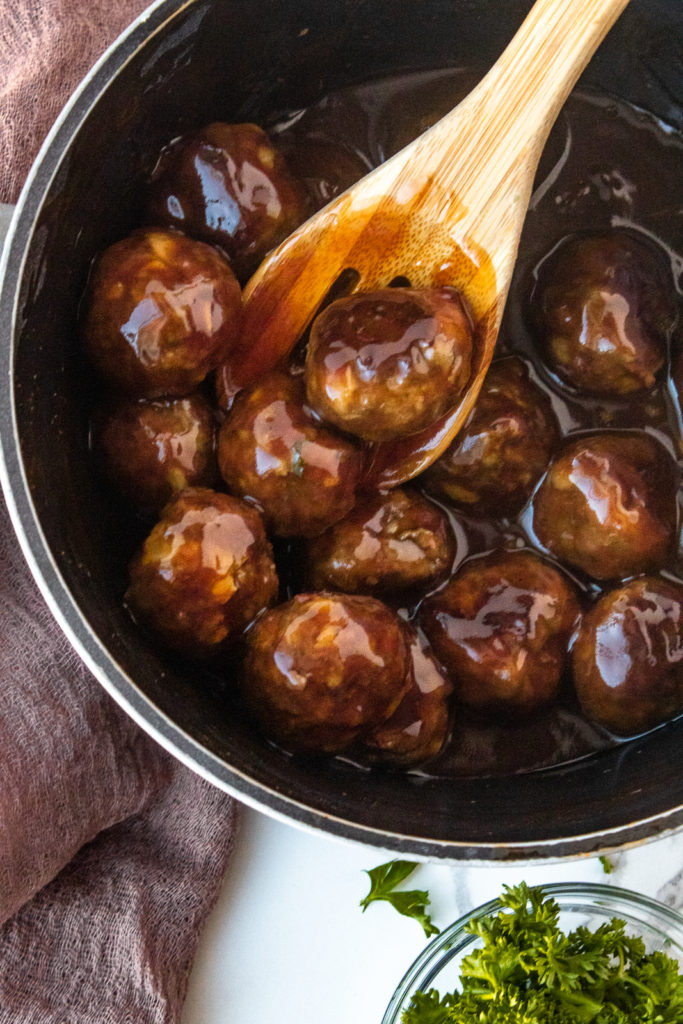 Easy basic meatballs in pot with Woden spoon in sweet n sour sauce overhead shot.