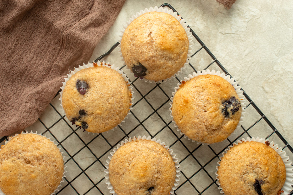 Healthy Blueberry Muffins Overhead shot on wire rack with brown linen beside.