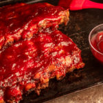 Slow Cooker BBQ Pork Ribs angled shot on baking pan with bbq sauce and pastry brush.