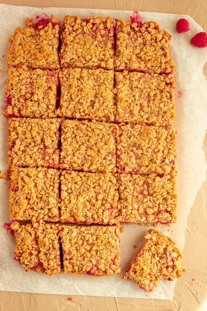 Raspberry Crumble Bars overhead shot cut into squares with one corner piece moved with bite.