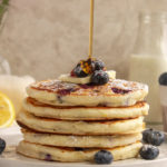 Lemon Blueberry Pancakes stacked on plate with syrup pour shot.