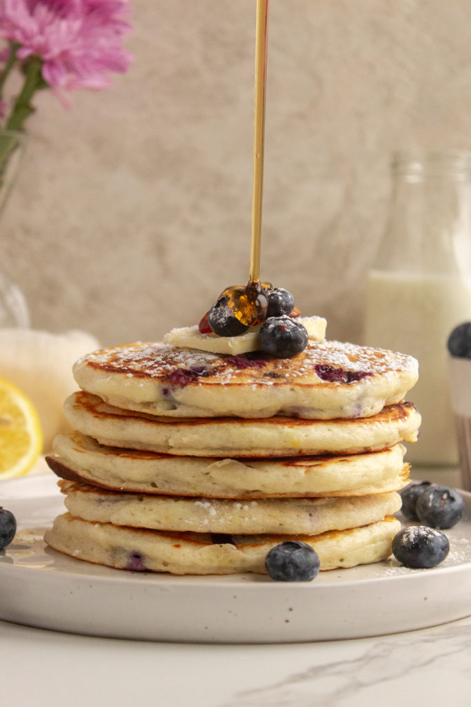 Lemon Blueberry Pancakes stacked on plate with syrup pour shot.