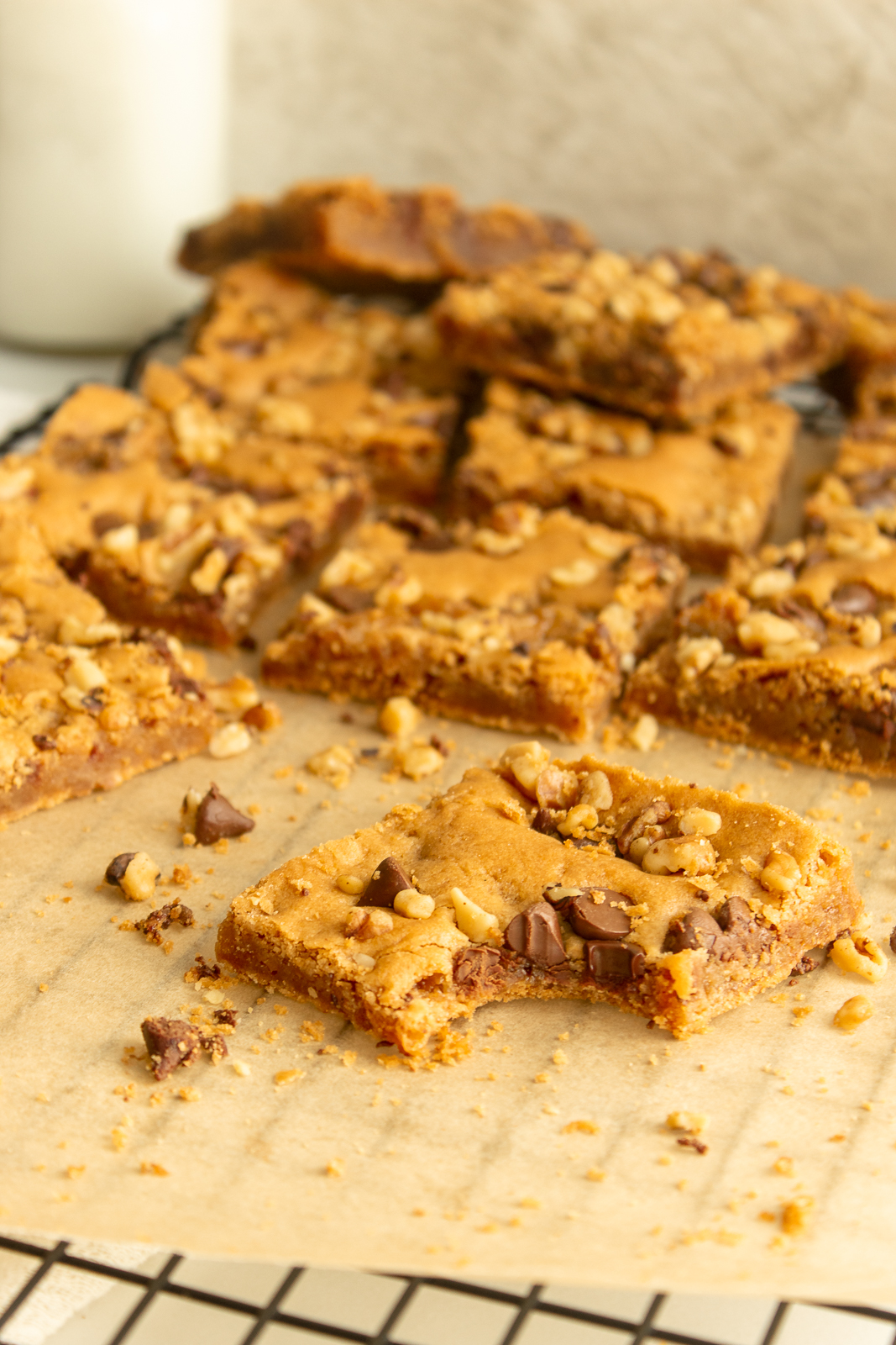 Chewy Nut Blondies on parchment paper on wire rack angled shot with a bite taken out.