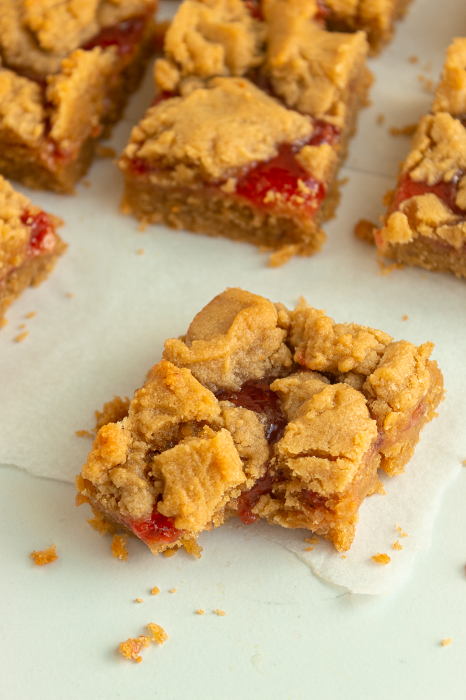 Peanut butter & jelly bars on parchment paper angled shot with a bite taken out.