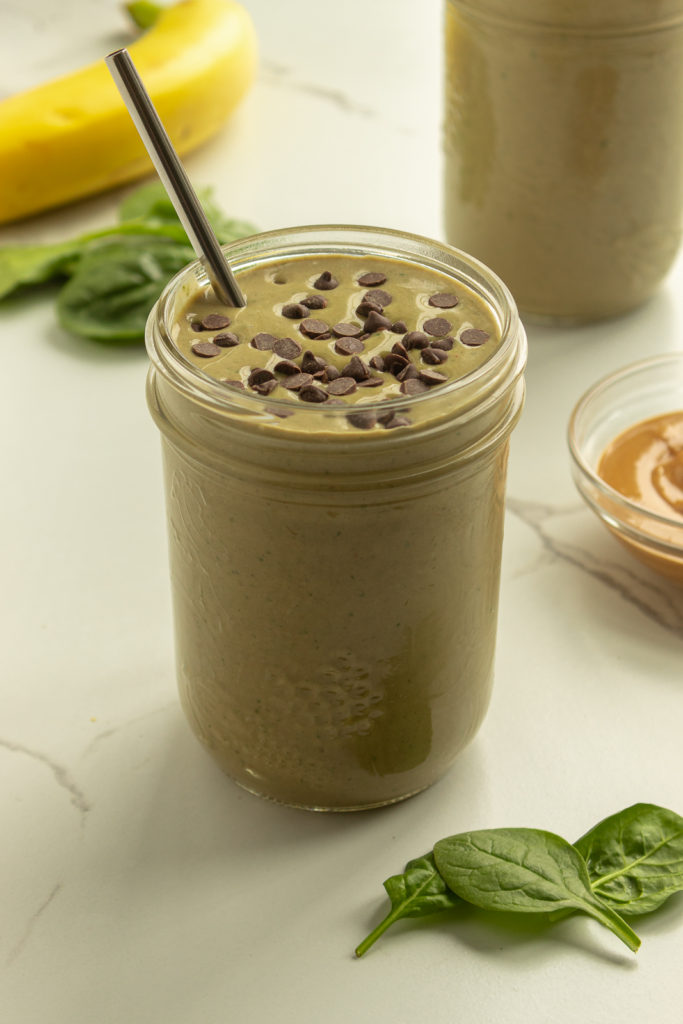 Angled shot of Chocolate Protein Green Smoothie in mason jar with straw and mini chocolate chips on top.