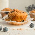 blueberry streusel muffins with paper cups with white backgrounds and surrounded by blueberries.