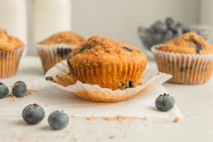 blueberry streusel muffins with paper cups with white backgrounds and surrounded by blueberries.