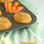 Carrot cake muffins in pan with carrots angled shot nada green cheesecloth.