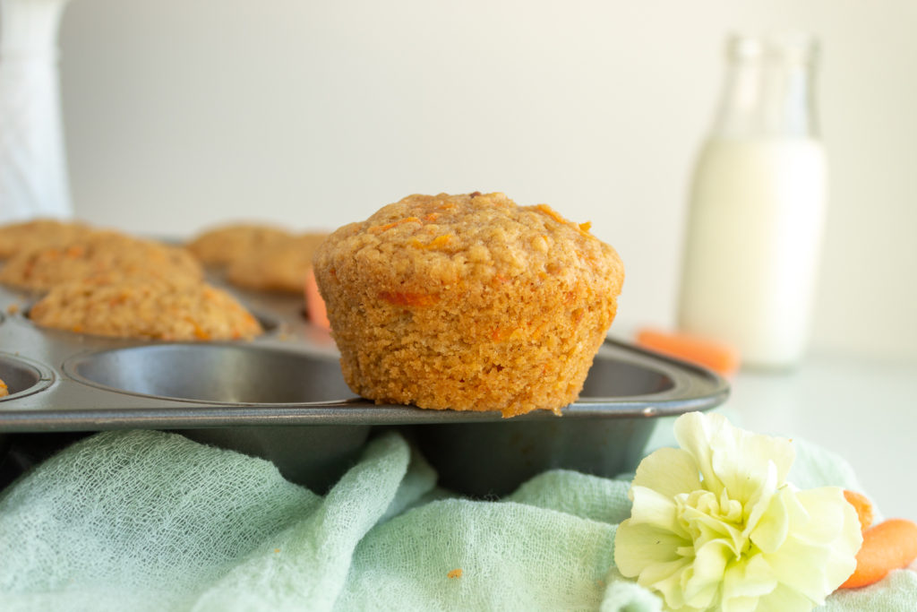 Carrot cake muffins straight on shot sitting on top of muffin pan with green cheesecloth in foreground.