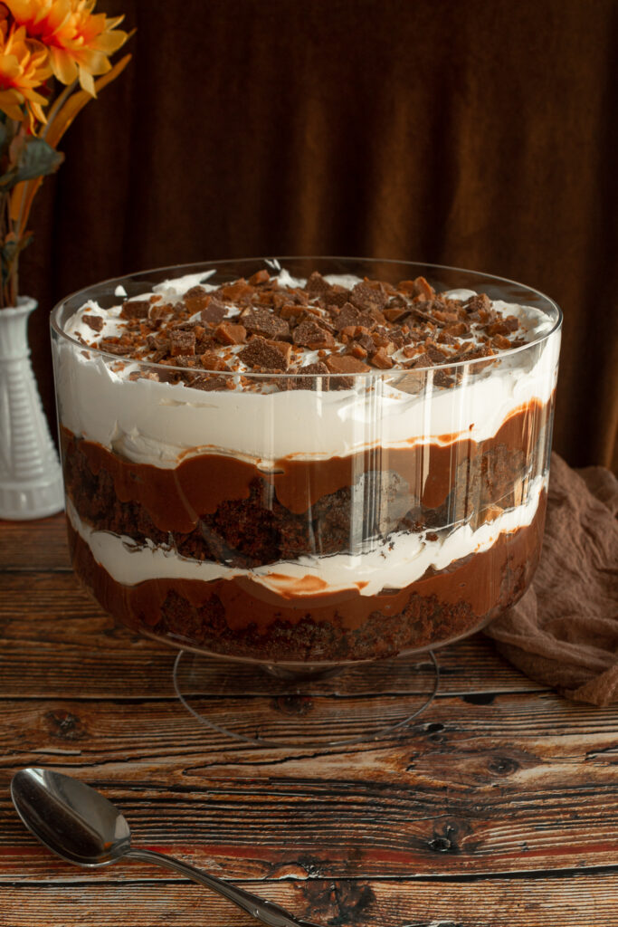 Death by Chocolate in trifle bowl with flowers in bakcground on wooden surface and spoon in foreground.