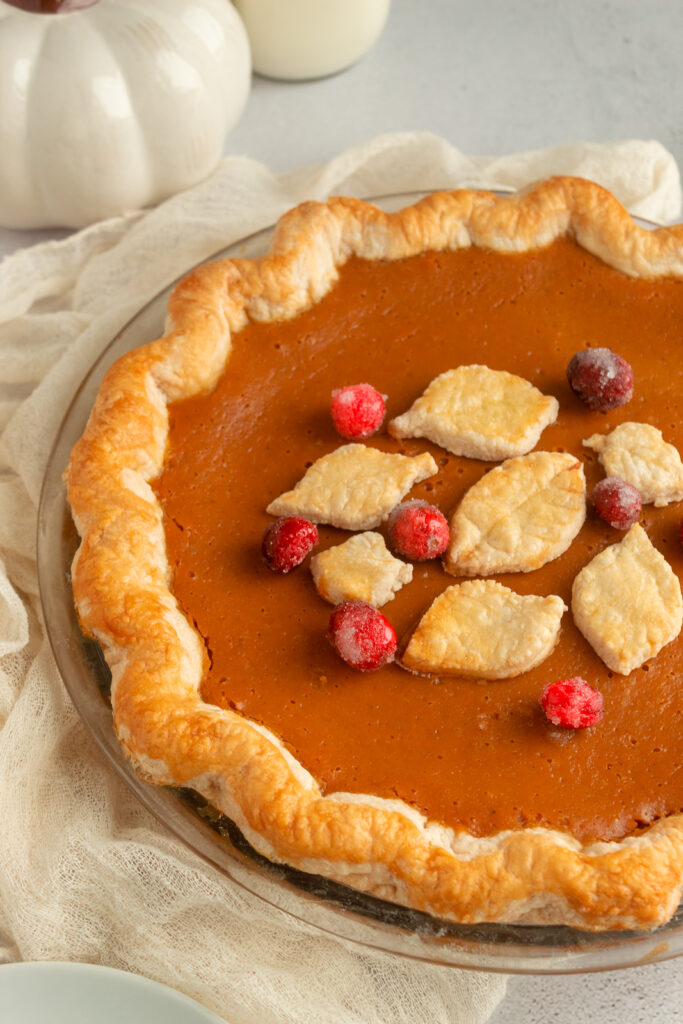 Pumpkin Pie Filling angled shot, whole pie in pie crust with sugared cranberries and poe crust leaves.